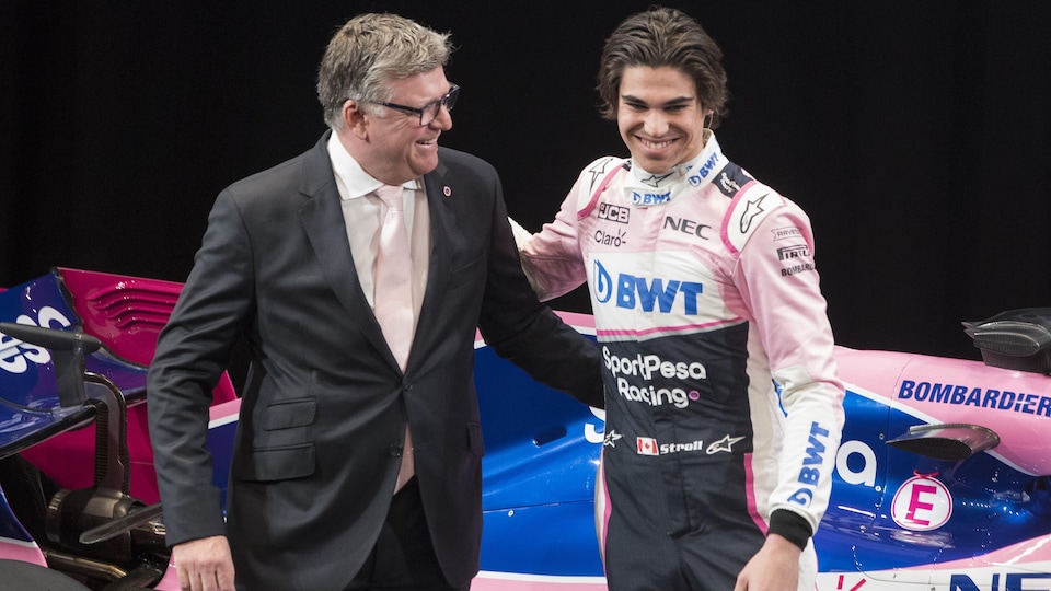 Devant une voiture, les deux hommes se font une accolade sur un podium devant les caméras.