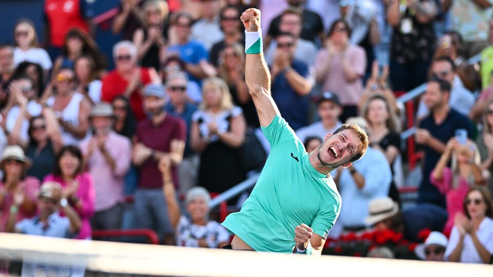Un joueur de tennis lève son poing droit en l'air en affichant un large sourire.