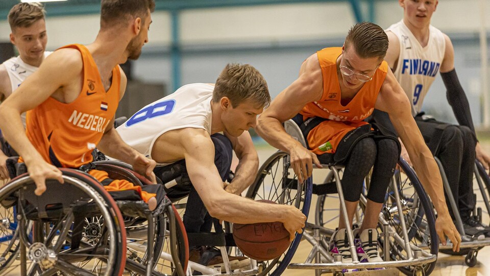 Des joueurs de la Finlande, en bleu, et des Pays-Bas, en orange, luttent pour le ballon dans un match de basketball en fauteuil. 