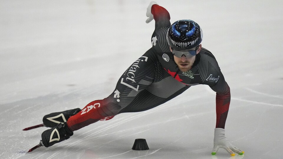 Un patineur de vitesse négocie un virage lors d'une compétition, la main gauche sur la glace.