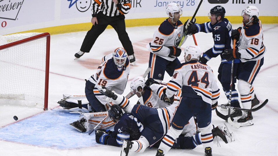 La rondelle glisse derrière le gardien sous le regard de quatre joueurs des Oilers.
