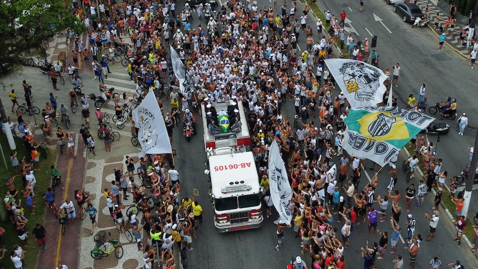 Un cercueil est hissé sur le haut d'un camion de pompiers, puis recouvert de deux drapeaux : celui du Brésil et celui du Santos FC.