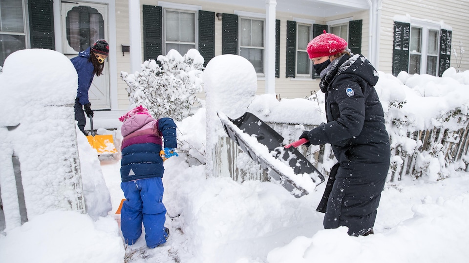 Une petite famille déneige le terrain de sa maison.