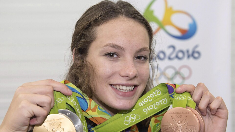 Elle porte ses quatre médailles olympiques à son cou.