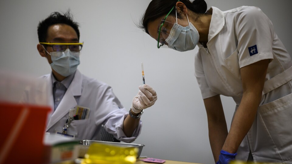 Un infirmier présente une seringue contenant une dose du vaccin contre la COVID-19 à une collègue.