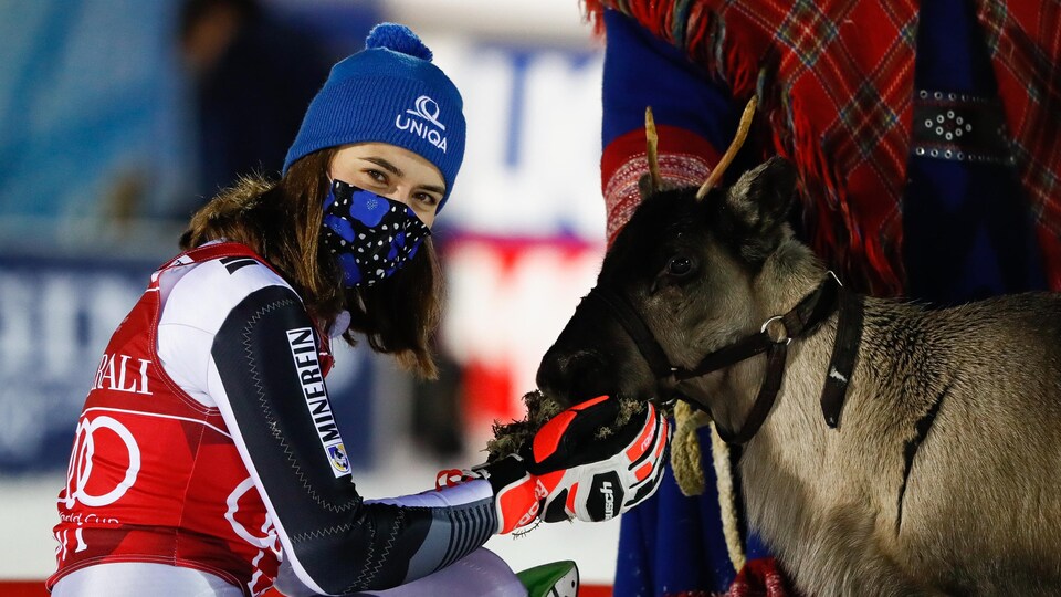La skieuse est agenouillée et caresse un renne.