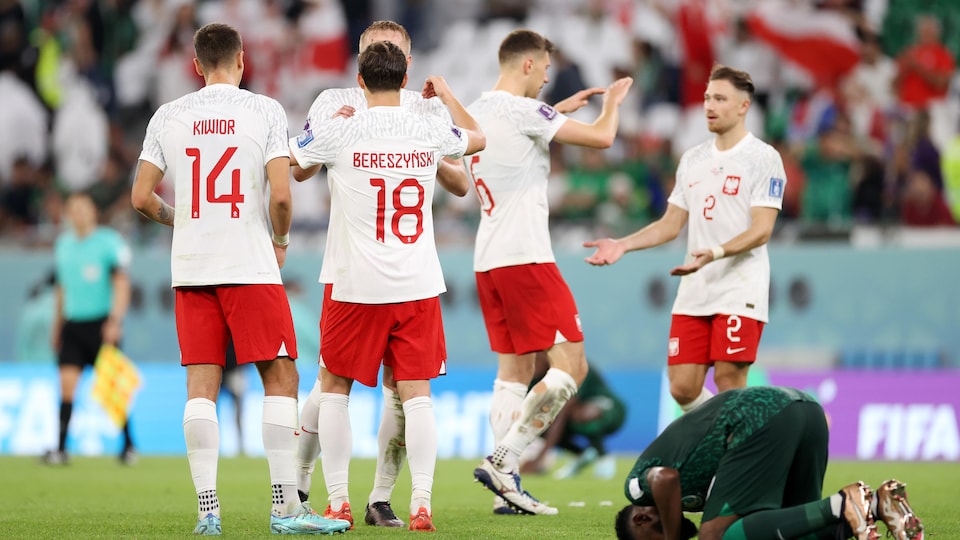 Des joueurs de soccer polonais se tapent dans les mains après une victoire alors qu'un joueur de l'Arabie saoudite est agenouillé le front contre le sol.