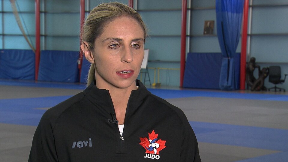 Une athlète avec un chandail noir et l'emblème de Judo Canada brodé donne une entrevue dans le dojo de l'INS-Québec.   