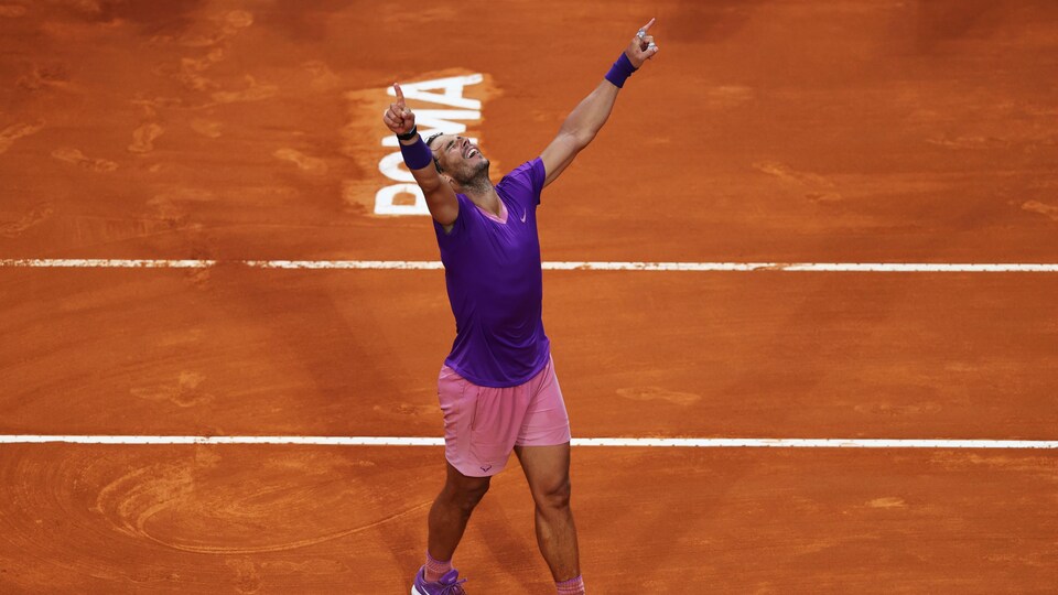 Un joueur de tennis, tout de mauve vêtu, lève les bras au ciel pour célébrer sa victoire.