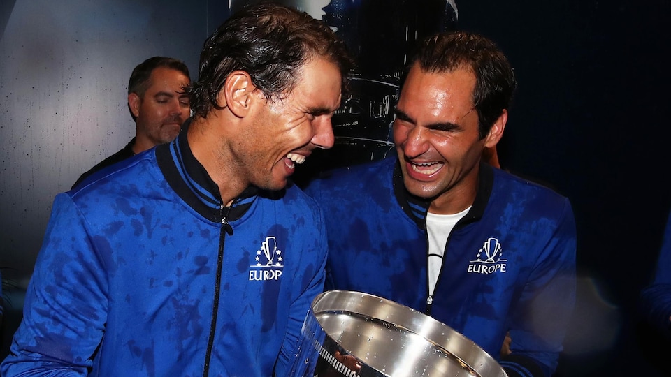 Two tennis players are laughing, one is holding a big trophy.
