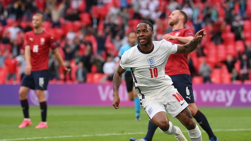Vêtu de l'uniforme blanc de l'Angleterre, il lève la main et s'apprête à sprinter vers le coin du terrain pour célébrer son but, tandis qu'en arrière-plan, deux joueurs tchèques sont dépités.