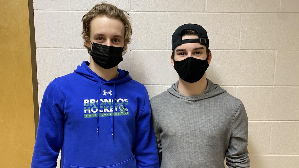 Les deux athlètes, portant le masque, posent devant un mur.