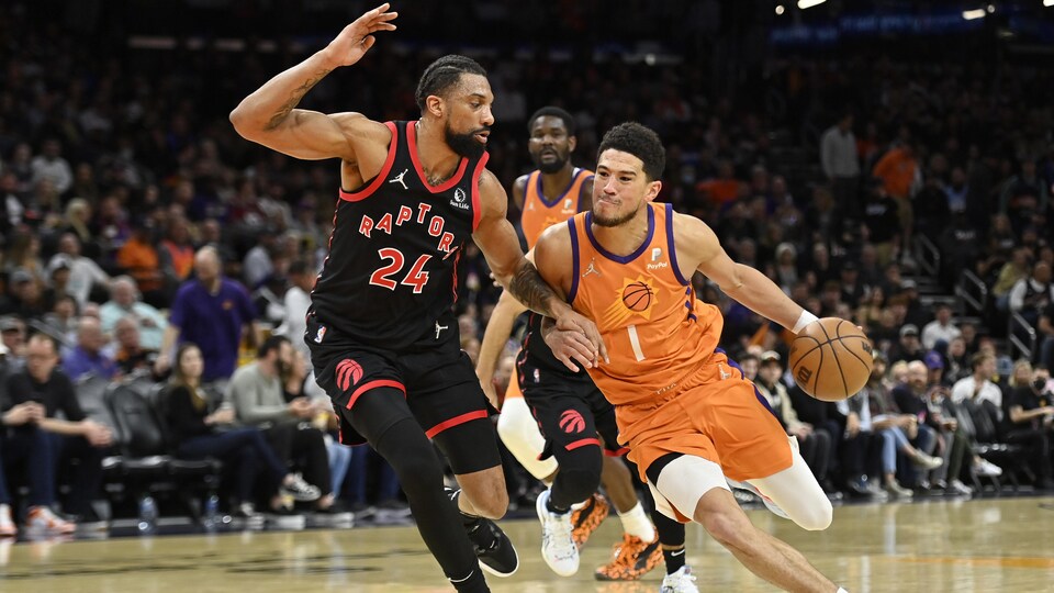 Le joueur des Raptors tente de bloquer celui des Suns qui tient le ballon dans sa main gauche.