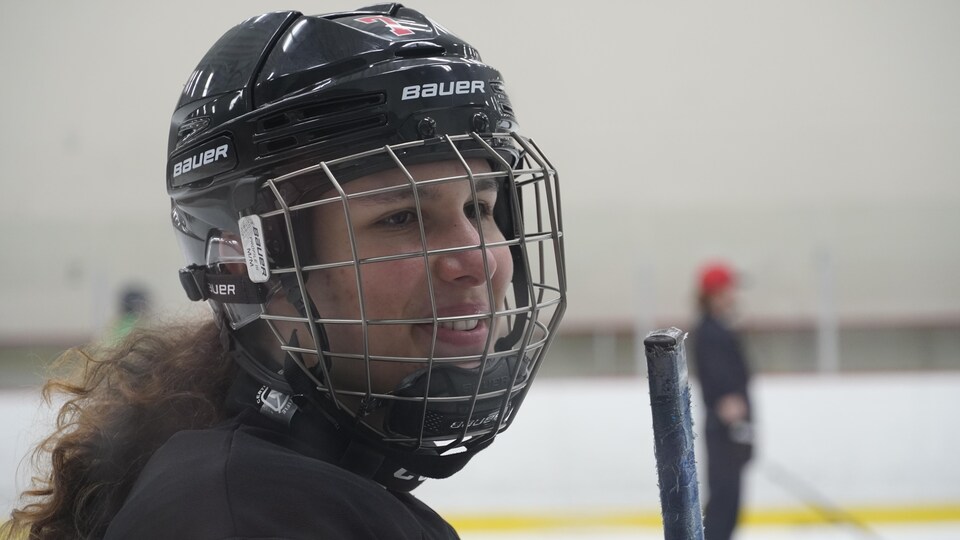Une jeune femme porte un casque avec grille pendant un entraînement de hockey.