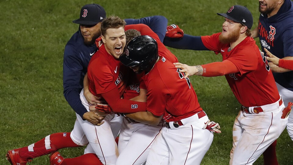 Des joueurs des Red Sox, vêtus de rouge, sautent sur leur coéquipier pour célébrer la victoire.