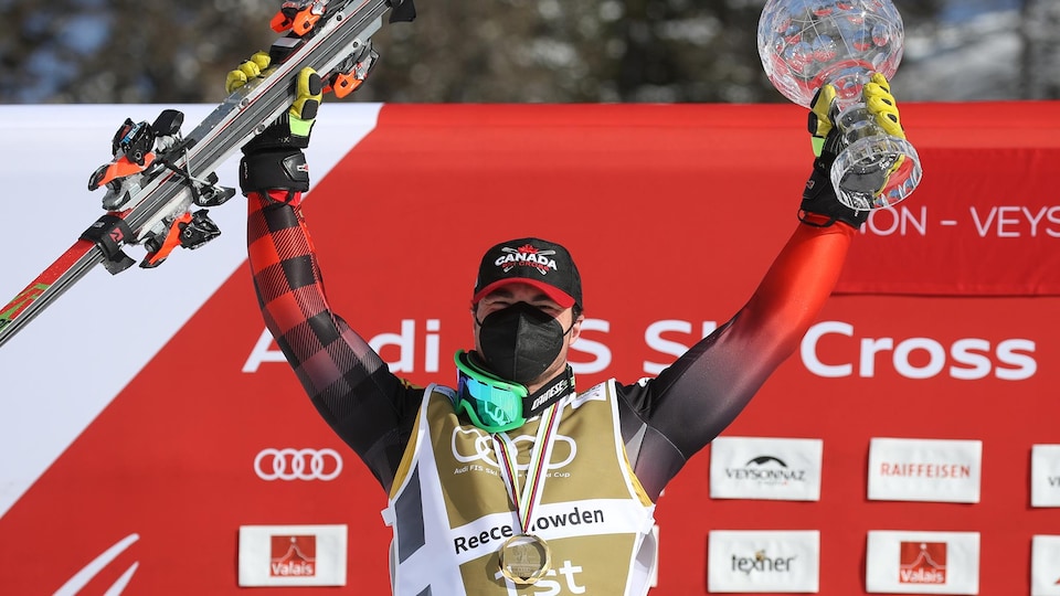 Un skieur tient ses skis dans une main et un trophée de l'autre.