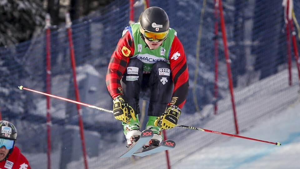 Un skieur vêtu de noir, de rouge et de vert descend un parcours de ski cross en Alberta.