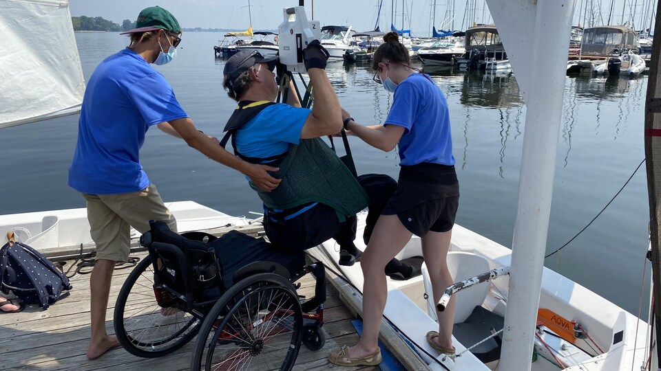Un homme est soulevé de son fauteuil roulant pour être assis dans un voilier.