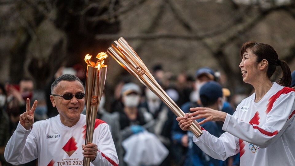 Deux sportifs tiennent le flambeau olympique.