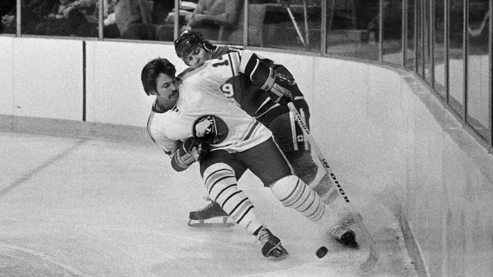 L'attaquant des Sabres, sans casque, tente de contrôler la rondelle le long de la bande contre un adversaire du Canadien de Montréal en 1977.