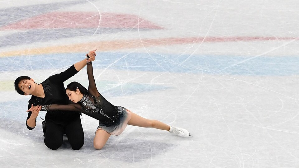 Un couple de patineurs artistiques est à genoux sur la glace pendant une performance.