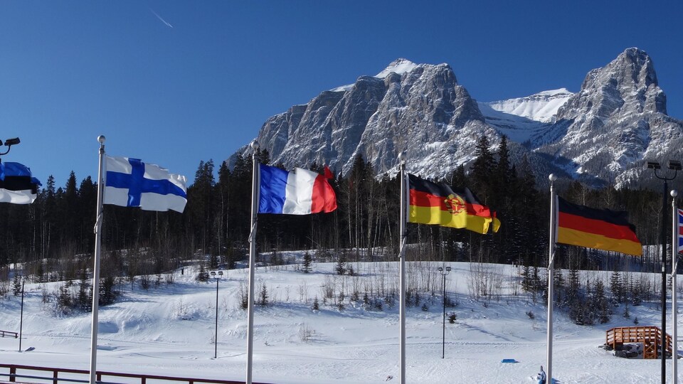 Des drapeaux de plusieurs pays flottent devant une chaîne de montagne.