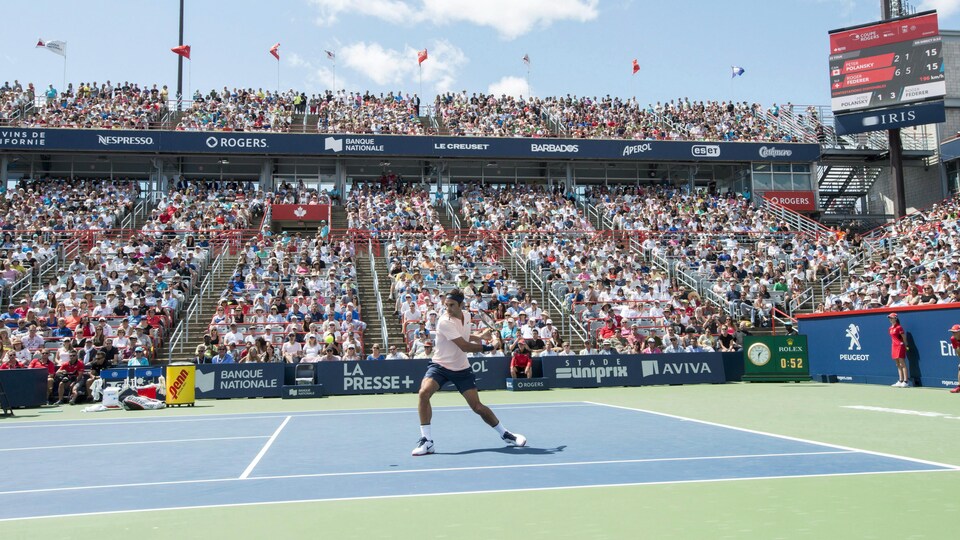 Dans un stade rempli, un joueur de tennis frappe la balle.