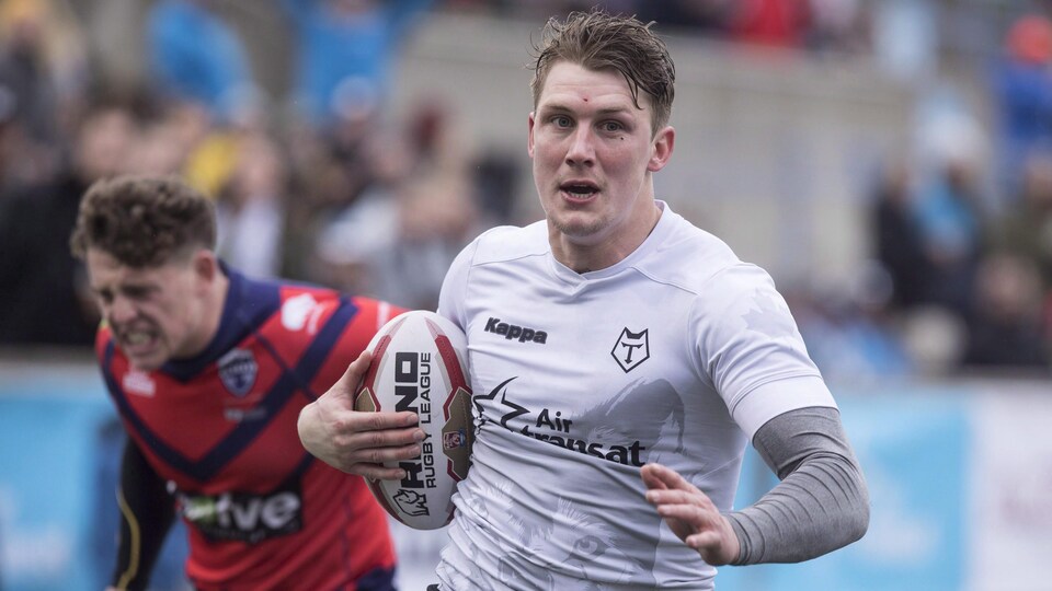 Un joueur de rugby court avec le ballon, poursuivi par un adversaire.