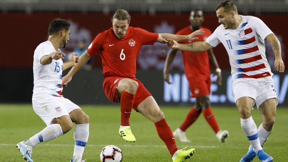 Le milieu de terrain du Canada Samuel Piette contrôle le ballon entre deux joueurs américains lors d'un match à Toronto. 