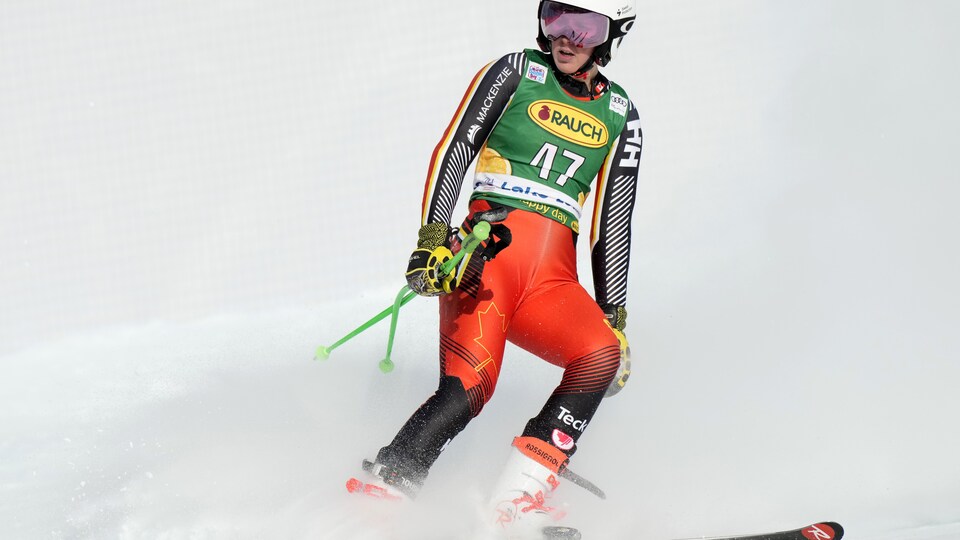 Une skieuse tient ses bâtons dans une main en descendant de côté une piste.