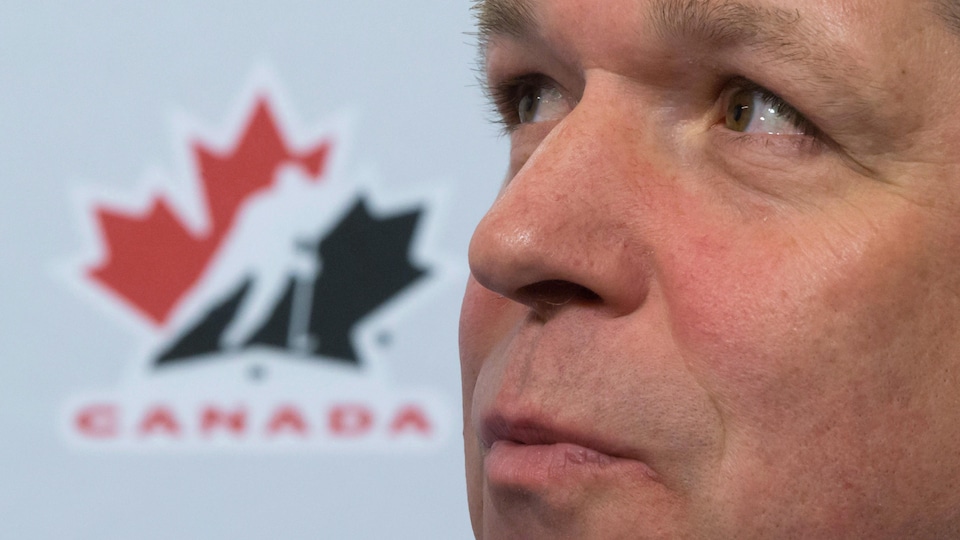 Il est photographié en gros plan devant un logo de Hockey Canada.