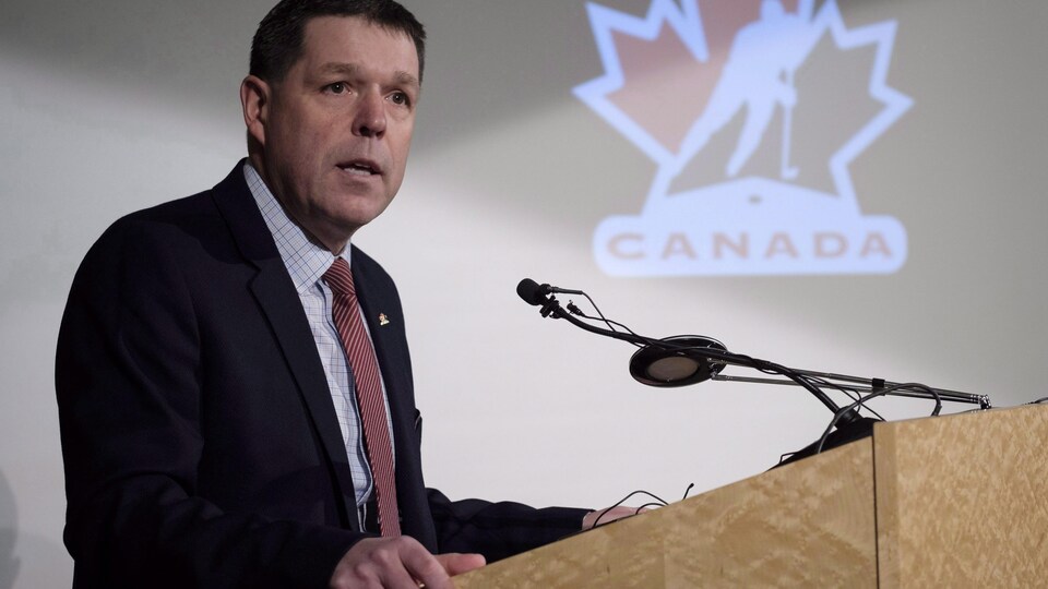 Il tient un discours devant un logo de Hockey Canada