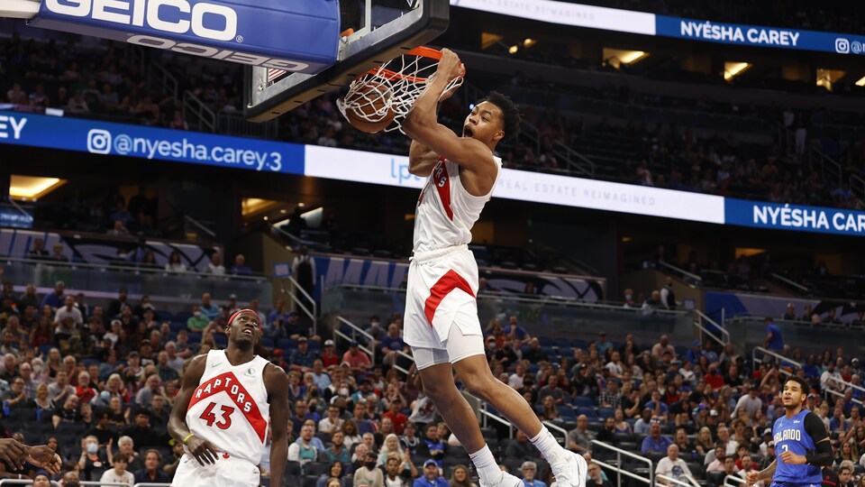 Le joueur de basketball tient le panier à deux mains, sous le regard attentif d'un coéquipier.
