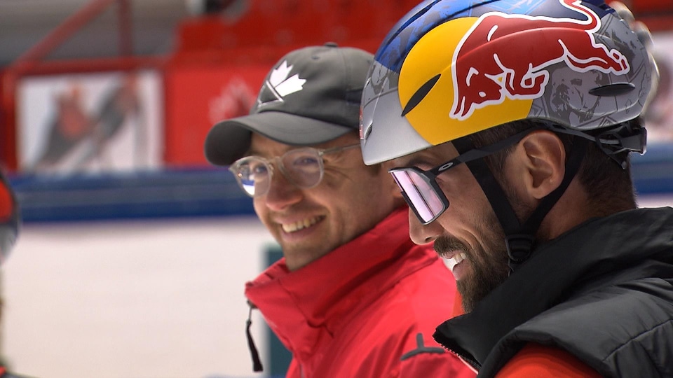 Un entraîneur et un patineur rigolent pendant un entraînement.