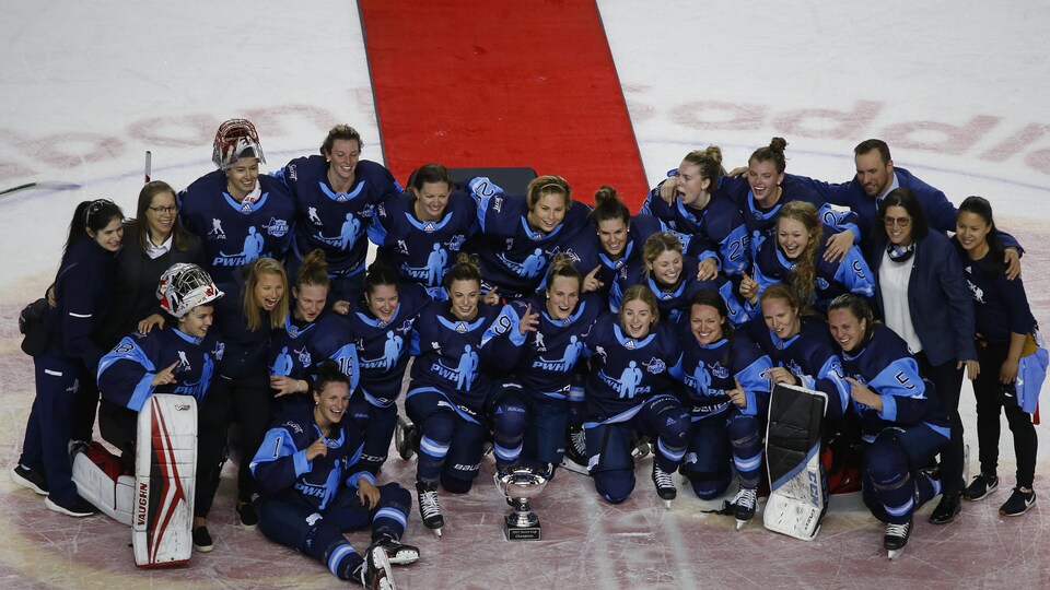 Les joueuses et les membres du personnel sont réunis au centre de la patinoire pour la photo protocolaire avec le trophée.