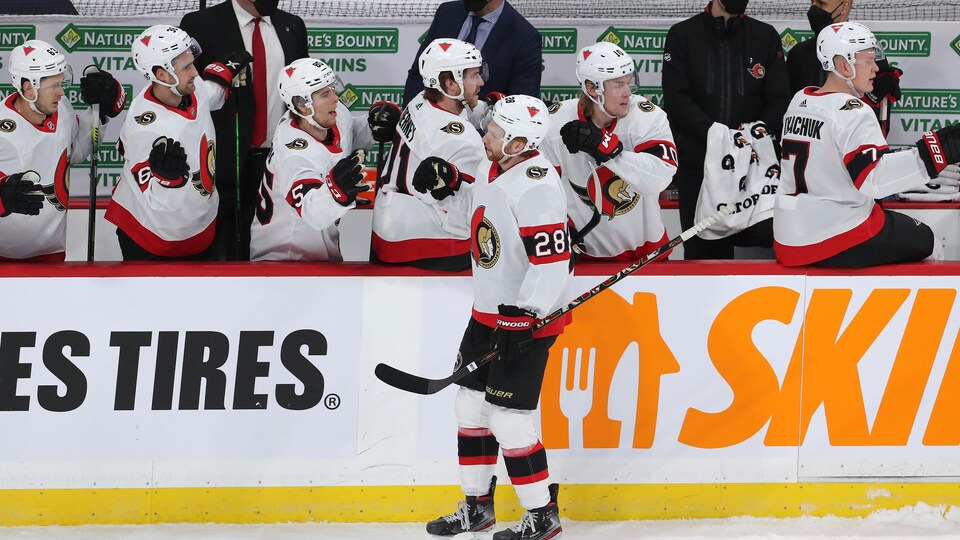 Des joueurs de hockey sont au banc de leur équipe et célèbrent un but avec leur coéquipier.