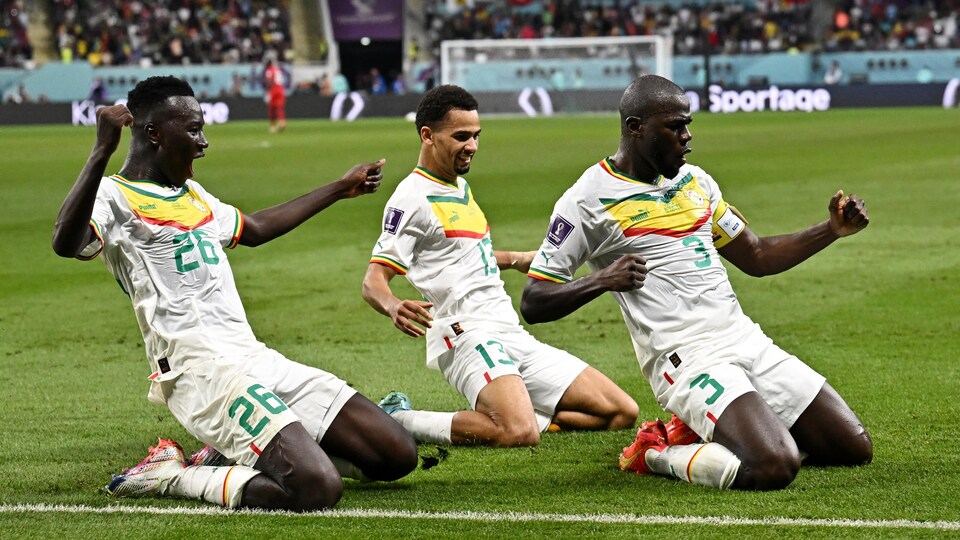 Trois joueurs sénégalais sont à genou sur le terrain pour célébrer le but. 