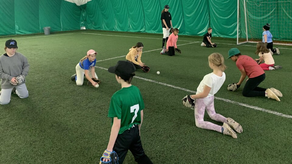 groupe de jeunes filles accroupies sur une surface synthétique échangeant un balle de baseball