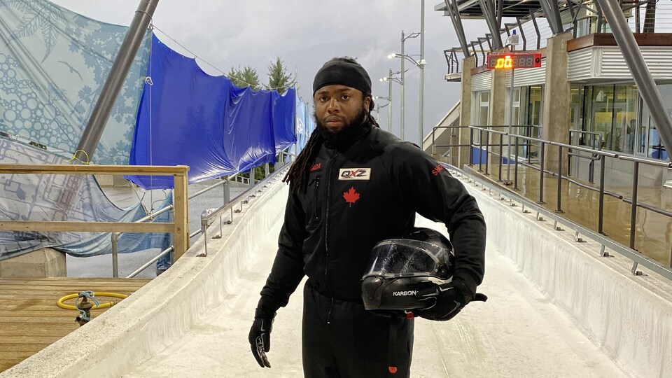 Shaquille Murray-Lawrence prend la pose avec son casque de bobeur au sommet d'une piste de bobsleigh.