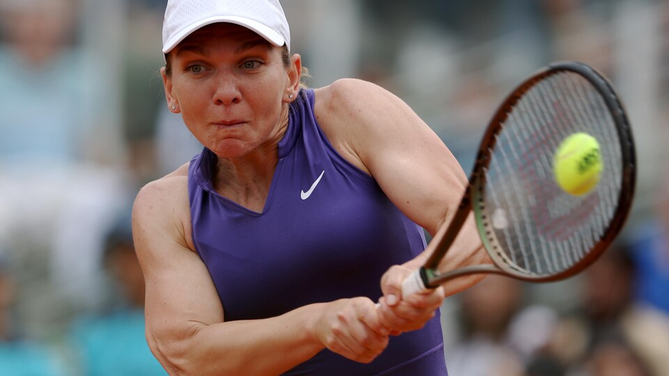 A tennis player, capped on his head, returns the ball with a two-handed backhand. 