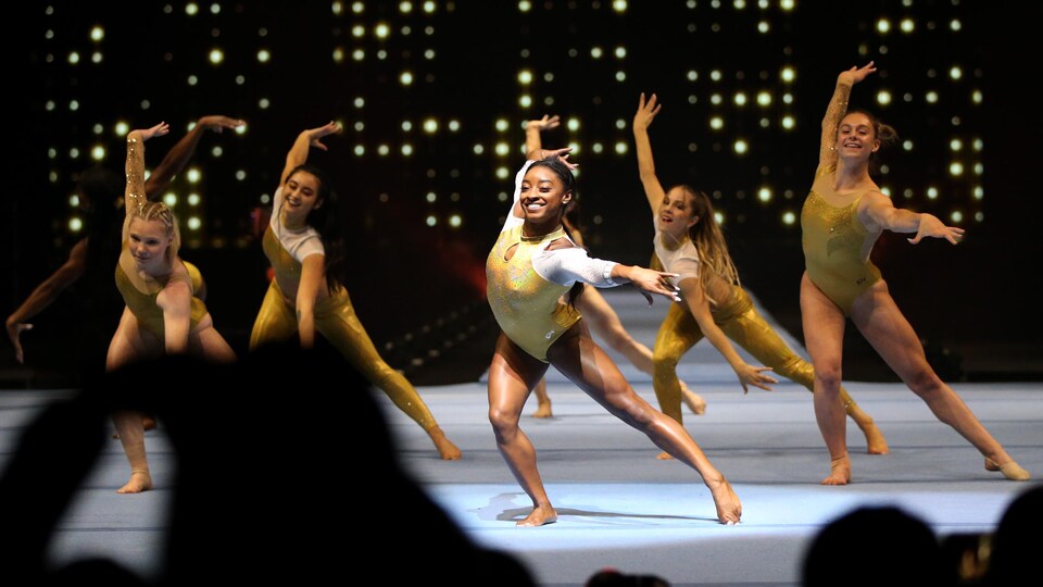 Des gymnastes vêtues d'uniformes dorés exécutent une chorégraphie devant des spectateurs.