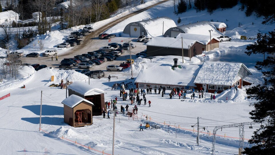 Vue en plongée d'un chalet de ski entouré de plusieurs skieurs, en hiver.