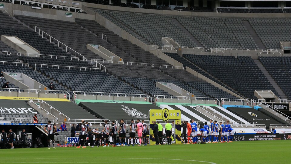 Des joueurs se tiennent debout sur la pelouse devant des tribunes vides.