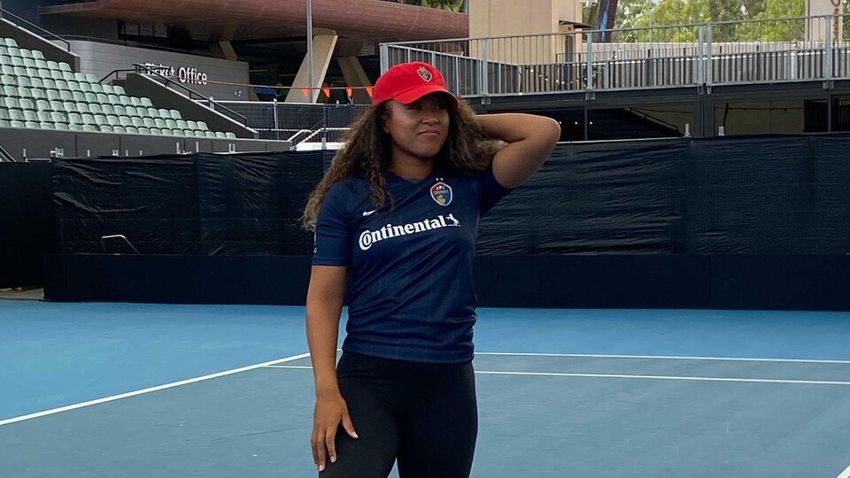 Elle prend la pose sur le court de tennis, un ballon de soccer sous le pied droit.