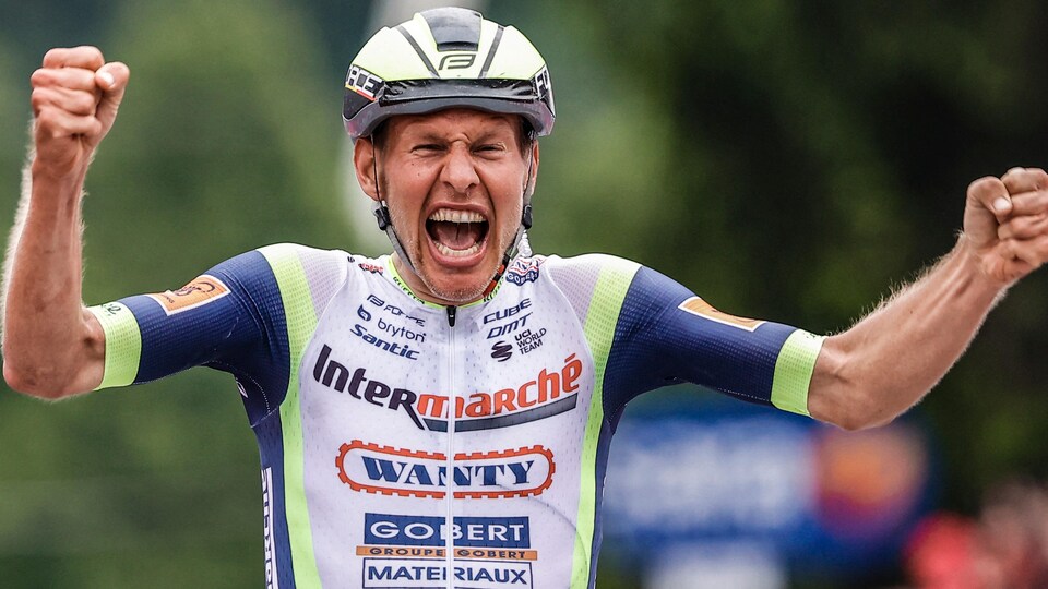 Le cycliste lève les bras et serre les poings tout en hurlant sa joie.
