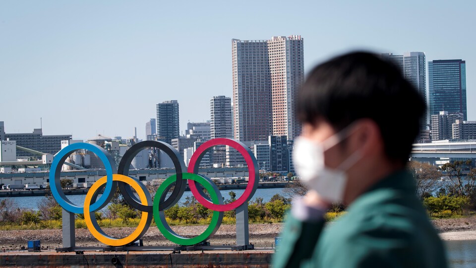 Un homme portant un masque marche devant les anneaux. olympiques à Tokyo.