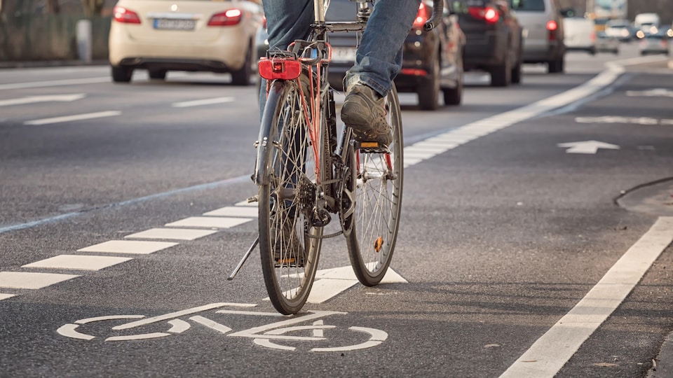 Un vélo qui circule sur une piste cyclable en ville avec des automobiles en fond.