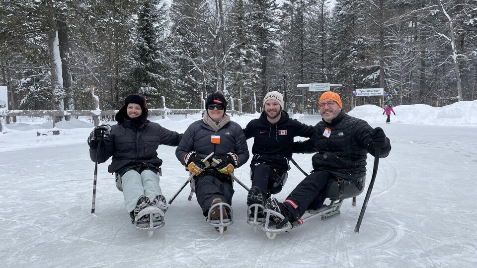 Quatre athlète de hockey sur luge prennent la pose sur une patinoire extérieure.