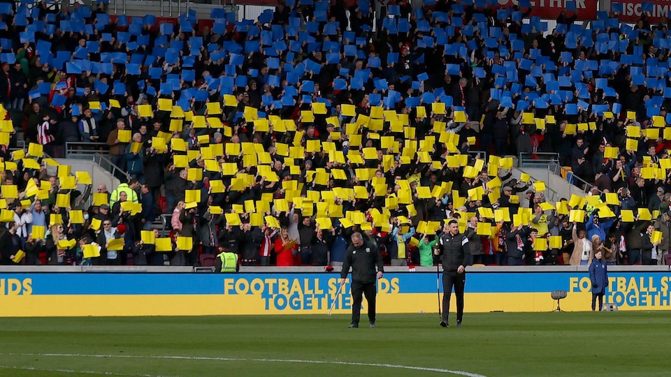 Fans are holding posters with the color of Ukraine on the stands of a soccer stadium.