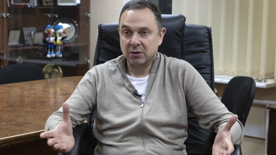 Assis sur un fauteuil dans un bureau, l'homme répond à une question.